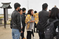 日和山の上で説明をする語り部と、閖上の町を見る留学生の写真
